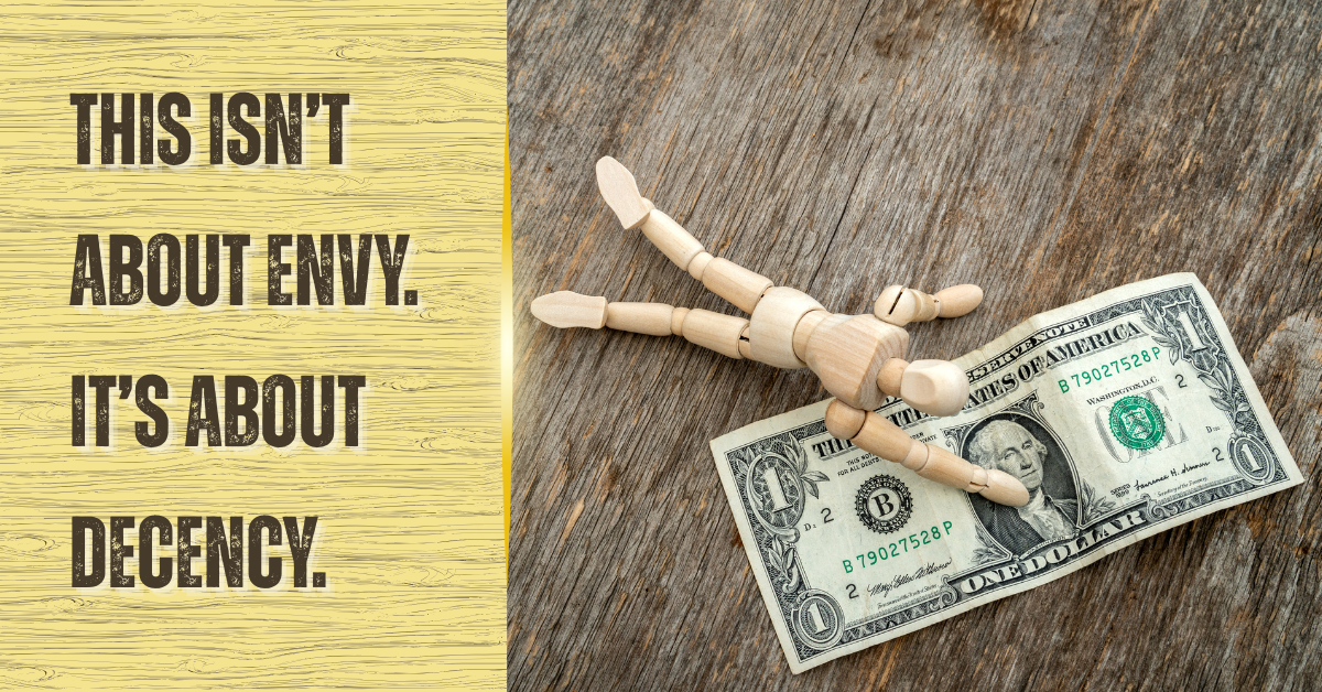 A wooden mannequin sprawled across a single dollar bill on a worn wooden surface. Beside it, bold black text on a yellow woodgrain background reads: “THIS ISN’T ABOUT ENVY. IT’S ABOUT DECENCY.”