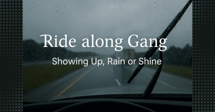 View through a rainy windshield on a highway, with a blurry semi-truck ahead and windshield wipers in motion. Overlay text reads: “Ride along Gang – Showing Up, Rain or Shine.”