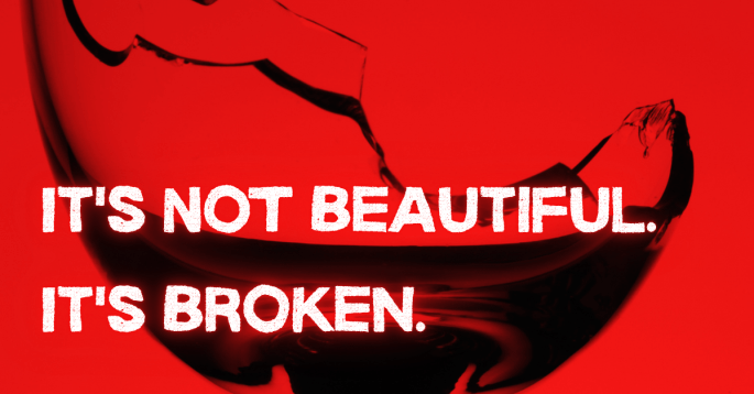 A close-up of a shattered wine glass against a bold red background. The jagged break runs sharply through the rim, symbolizing damage and danger. Overlaid in bold white text are the words: “IT’S NOT BEAUTIFUL. IT’S BROKEN.”