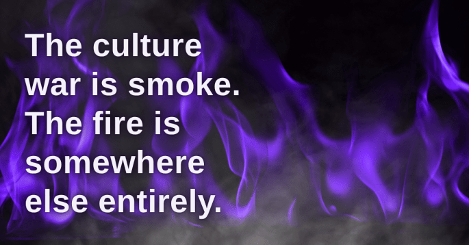 Purple flames rise against a dark background, blending with light smoke in the foreground. Bold white text overlays the image, reading: “The culture war is smoke. The fire is somewhere else entirely.” The visual evokes a sense of distraction masking deeper danger.