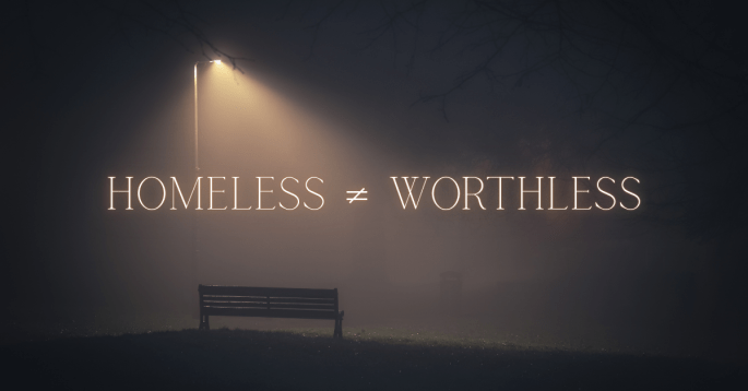 A dark, foggy park scene with a single empty bench under the glow of a lone streetlamp. Large illuminated text across the image reads “HOMELESS ≠ WORTHLESS,” emphasizing the dignity and humanity of people experiencing homelessness.