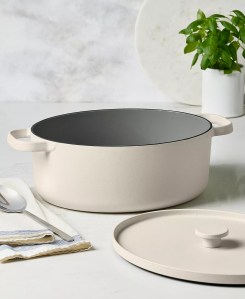 Neutral-toned enameled Dutch oven with lid placed beside it on a light kitchen surface.