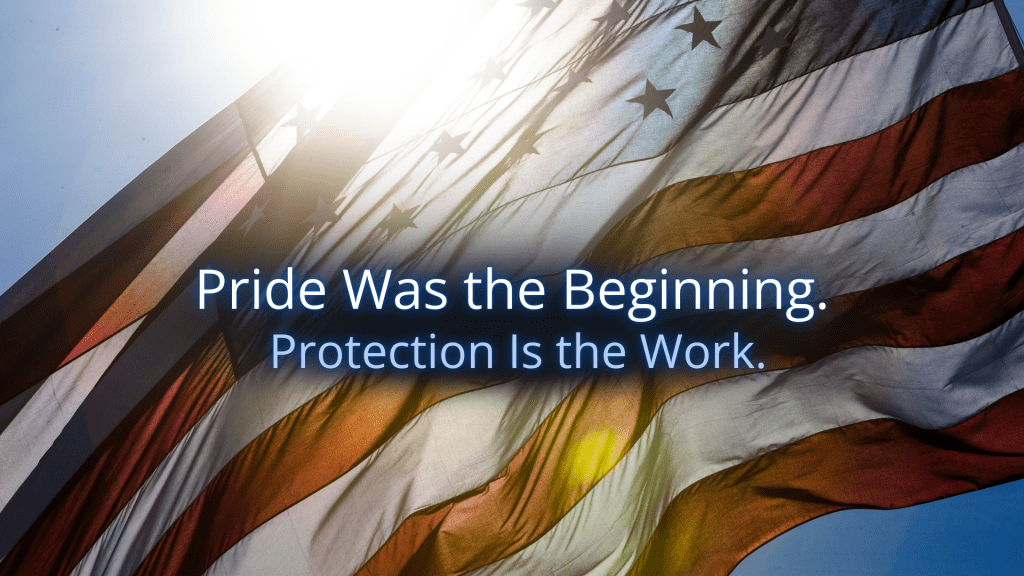 American flag waving in sunlight with the words “Pride Was the Beginning. Protection Is the Work.” centered in soft blue text.