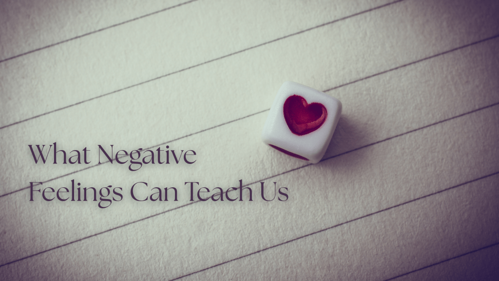 Feature image with the title “What Negative Feelings Can Teach Us” over a softly lit sheet of lined paper, beside a small white cube with a red heart on one side.