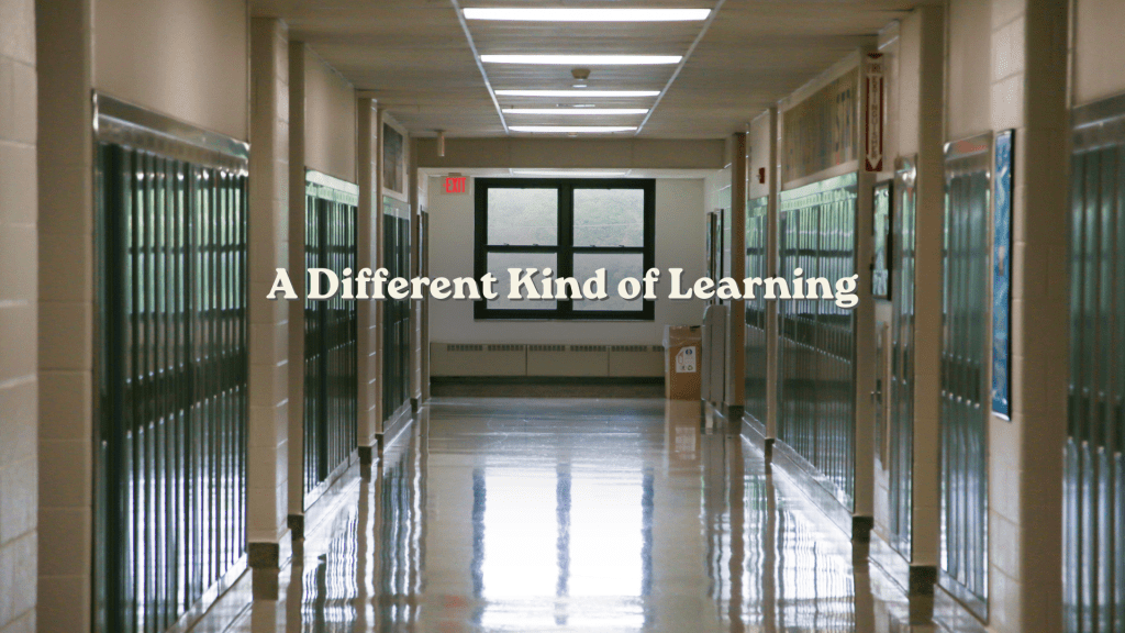 Empty high school hallway lined with dark lockers, with soft natural light at the far end and the title “A Different Kind of Learning” centered in cream serif text.