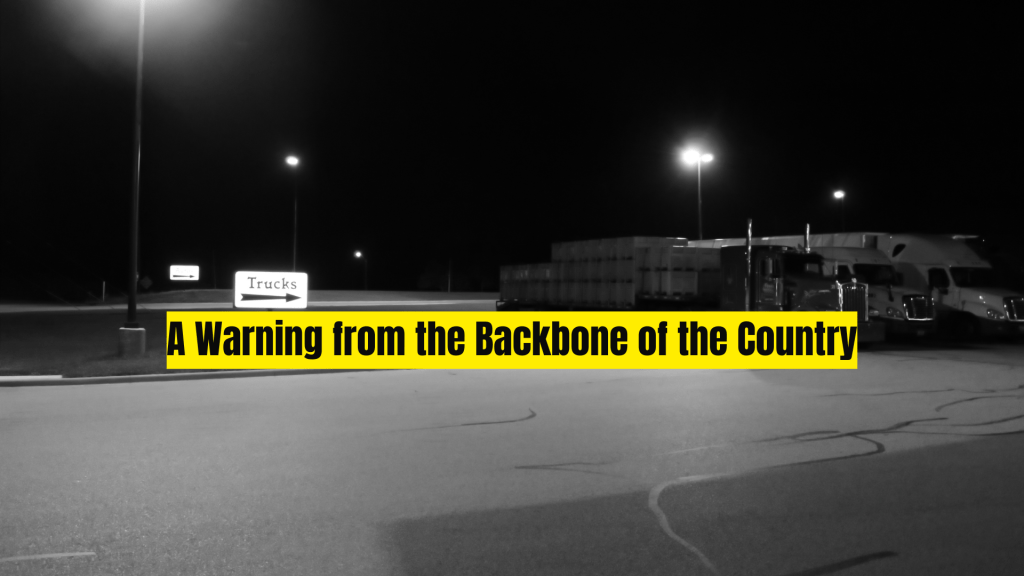 Black-and-white night scene of a quiet truck stop with parked semis, glowing overhead lights, a “Trucks” sign, and yellow overlay text reading, “A Warning from the Backbone of the Country.”
