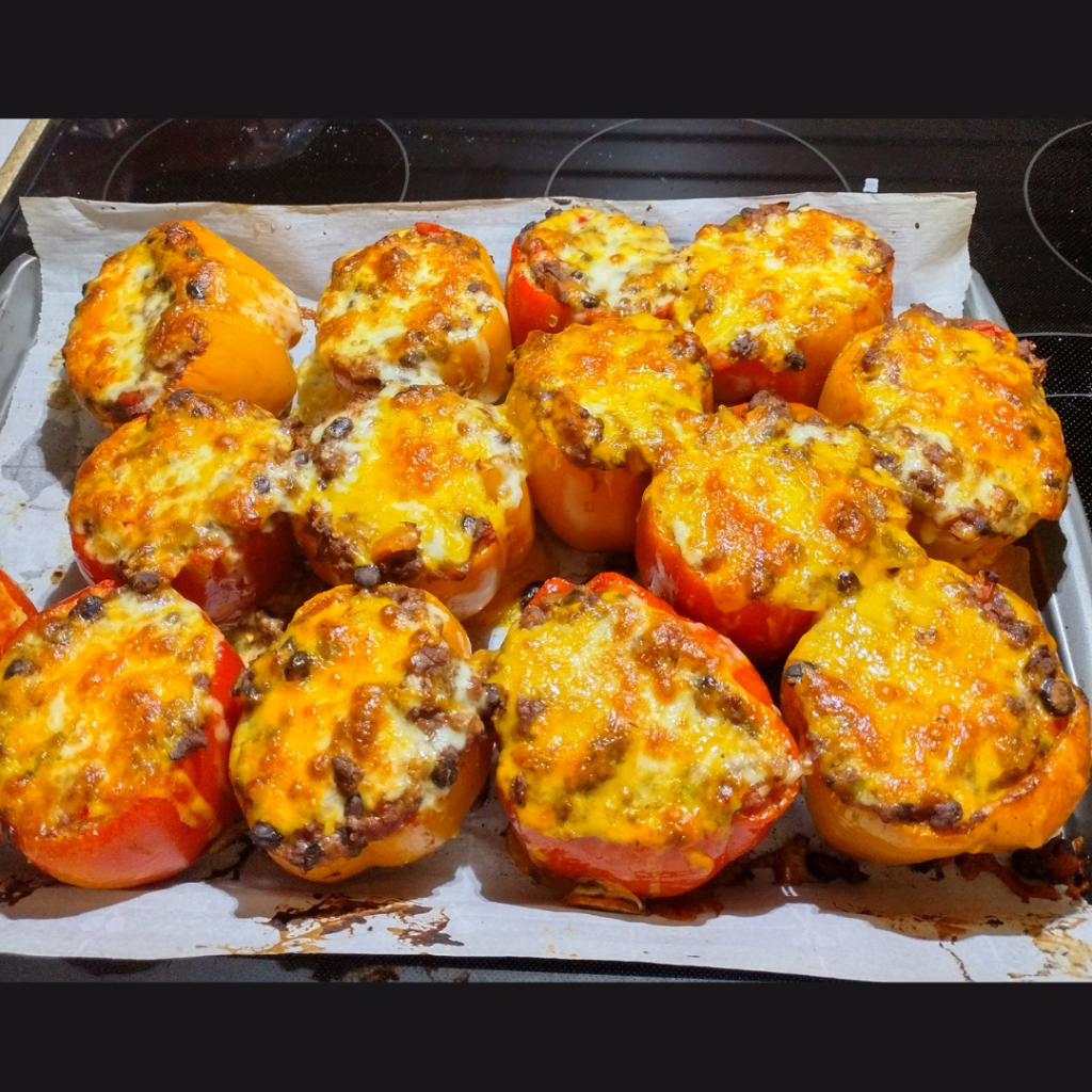 Red and orange bell peppers stuffed with taco-style ground beef and black bean filling, topped with melted cheese, and baked on a parchment-lined sheet pan.