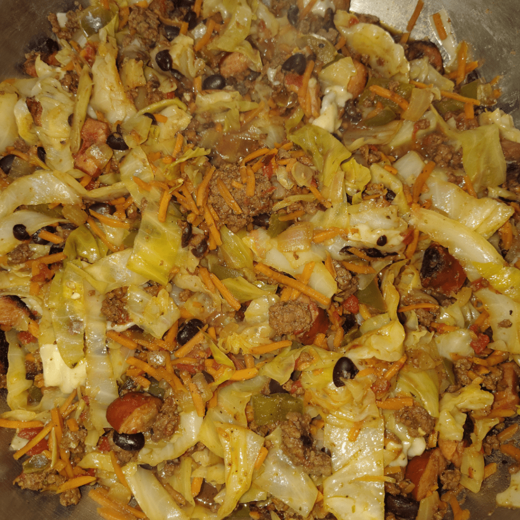 Dirty cabbage variation with cabbage, shredded carrots, black beans, tomatoes, onions, peppers, ground beef, and sliced apple gouda sausage cooking together in a pan.