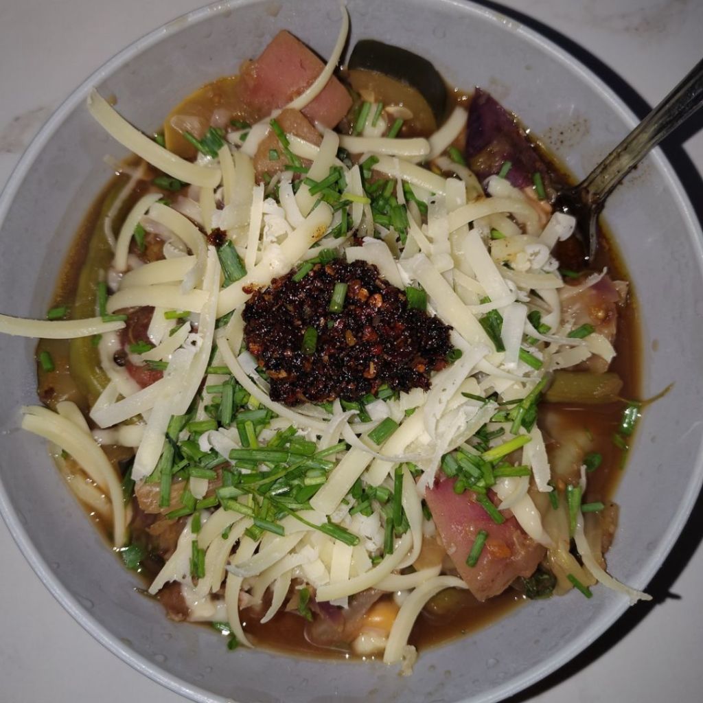 A bowl of Cherry Soup: Late Summer Harvest topped with freshly grated Parmesan, chopped chives, and garlic chili oil, served after a day of cooking with locally sourced vegetables and herbs.