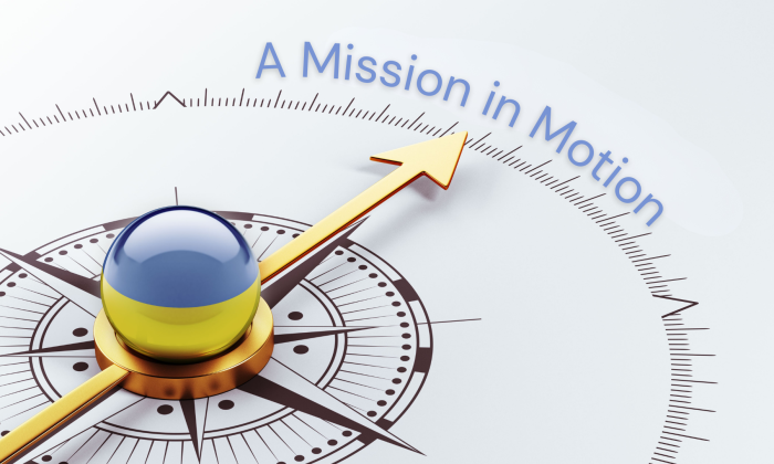 A compass illustration with a golden arrow pointing forward and a blue-and-yellow glass center, symbolizing direction and forward movement. The words “A Mission in Motion” arc above the compass on a light background.