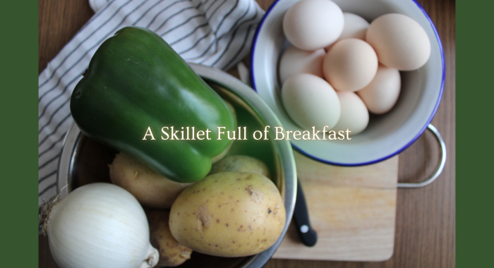A green pepper, onion, potatoes, and a bowl of eggs arranged on a kitchen surface with the overlay text “A Skillet Full of Breakfast.”