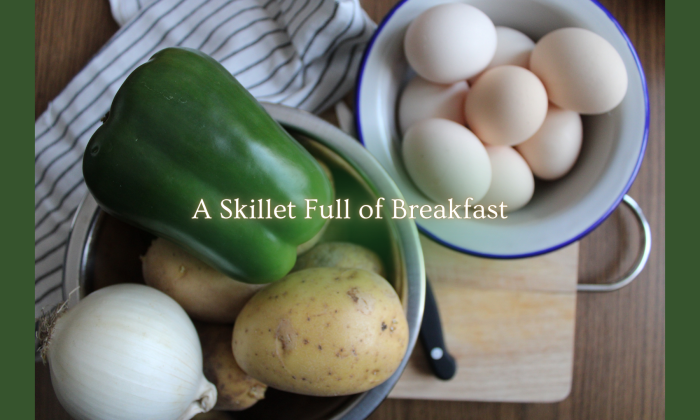 A green pepper, onion, potatoes, and a bowl of eggs arranged on a kitchen surface with the overlay text “A Skillet Full of Breakfast.”
