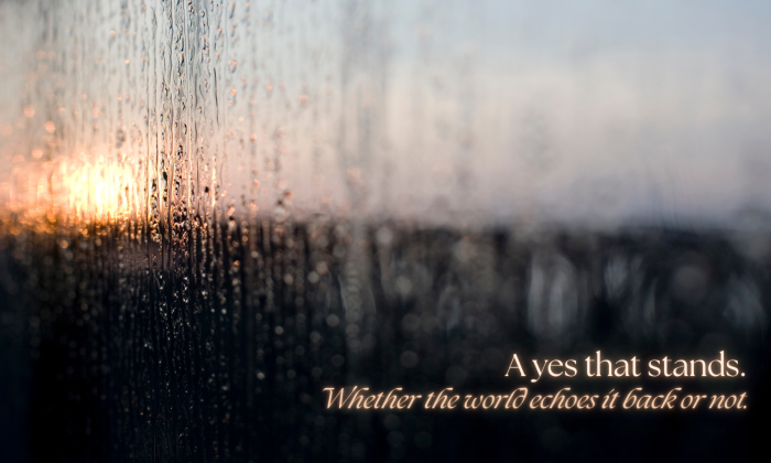 Rain-streaked window glowing with warm sunrise light beyond the glass. Overlay text reads: “A yes that stands. Whether the world echoes it back or not.”
