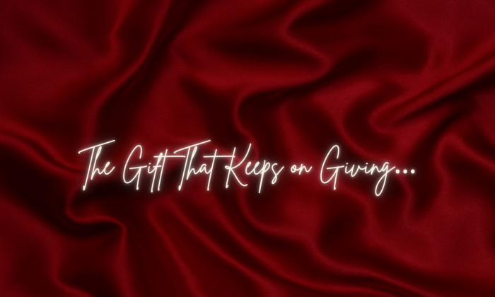 Deep red fabric softly folded, with white handwritten-style text reading “The Gift That Keeps on Giving…”