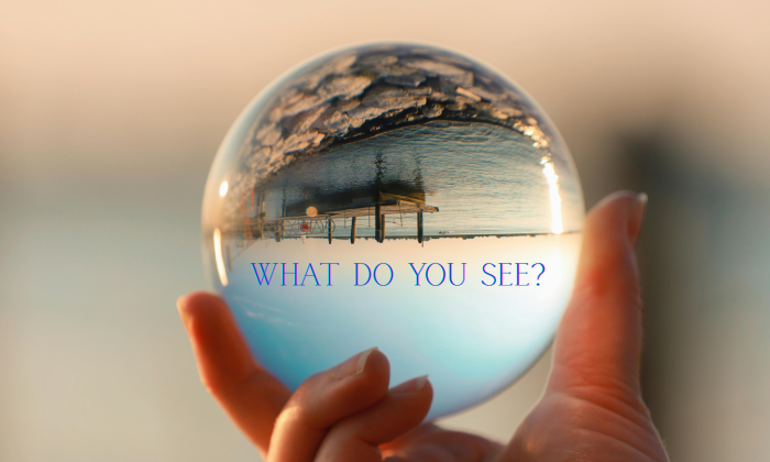 A hand holding a glass sphere that reflects an upside-down landscape, symbolizing perception and fractured reality, with the text “What do you see?”
