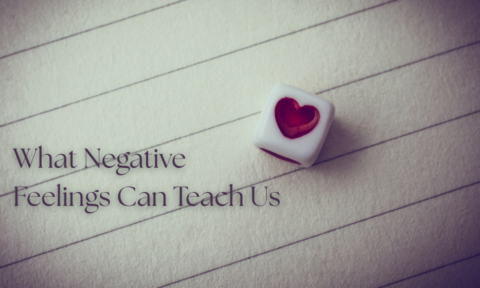 Feature image with the title “What Negative Feelings Can Teach Us” over a softly lit sheet of lined paper, beside a small white cube with a red heart on one side.