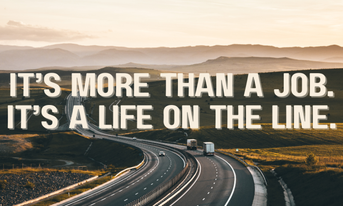 A lone highway curves through open fields at sunset, two trucks traveling side by side. Text overlay reads: "It’s More Than a Job. It’s a Life on the Line."